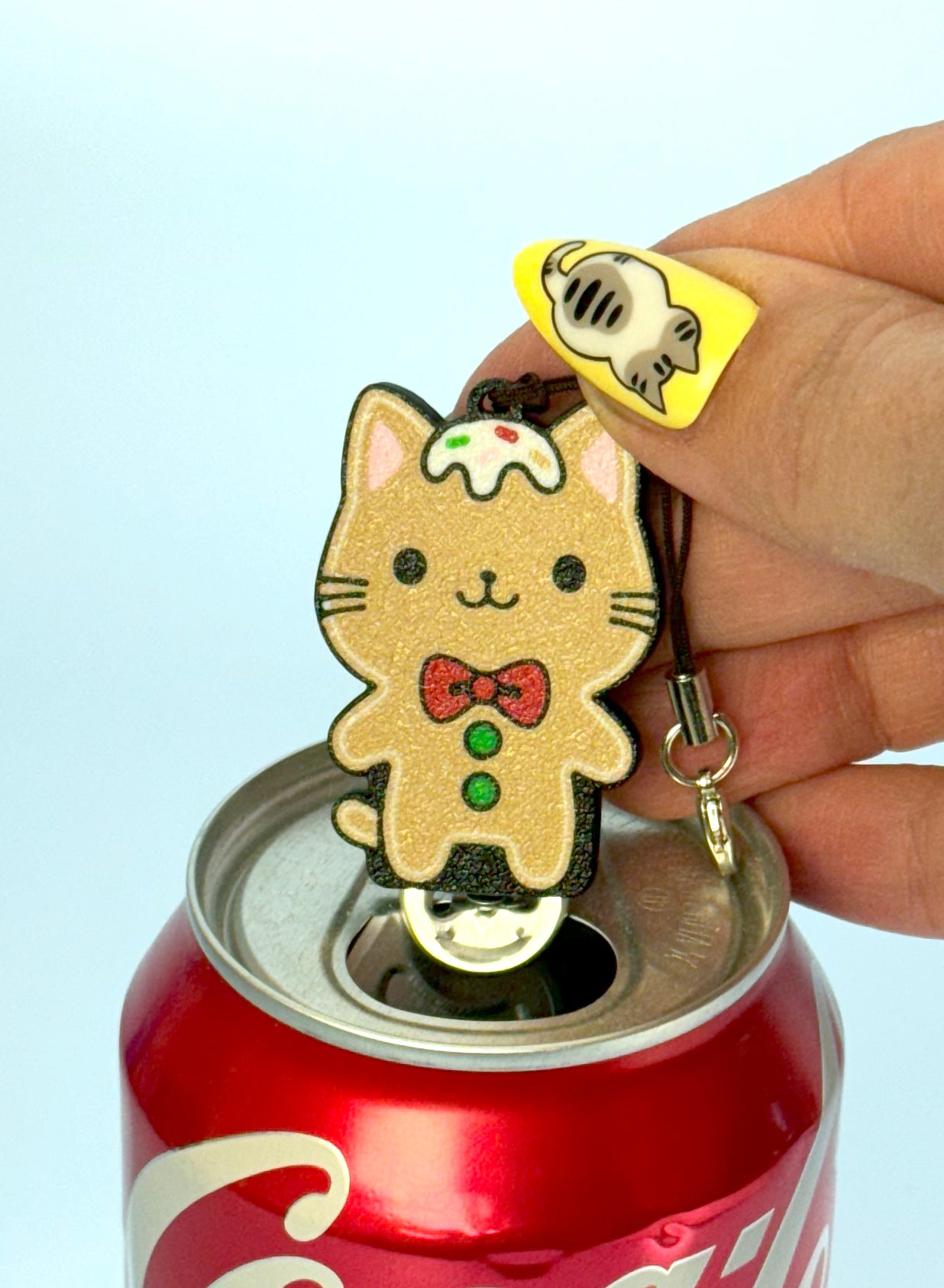 Hand holding a cat-shaped Gingerbread Tab Buddy with a bow tie and frosting with sprinkles on its head on a can of pop.