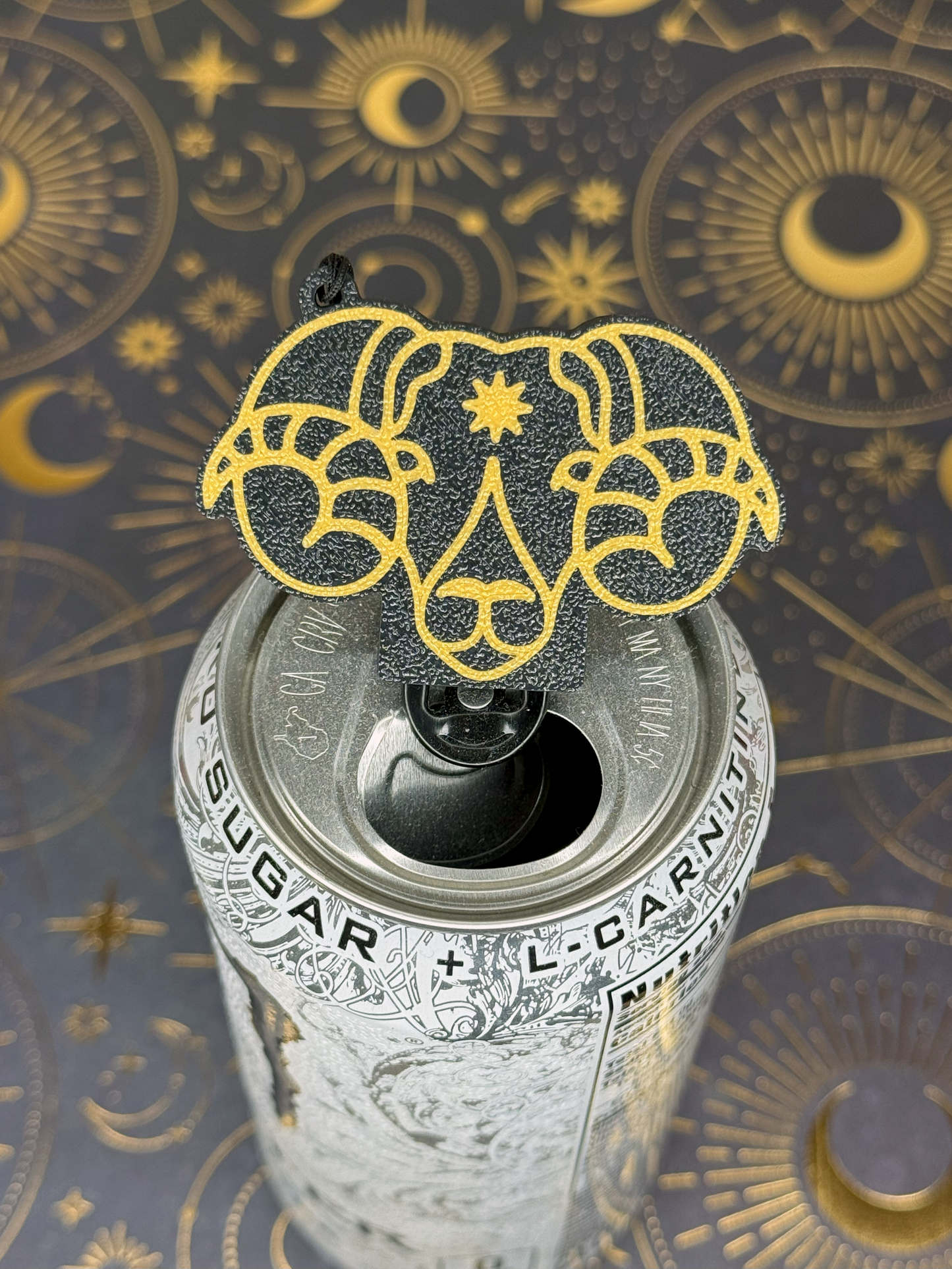 Can of energy drink with a ram's head Aries Tab Buddy design on top against a celestial pattern background