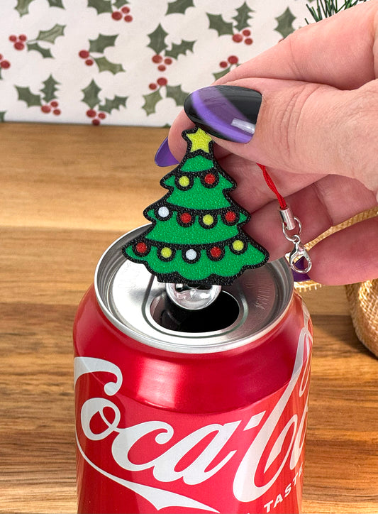 Hand holding a Christmas tree-shaped Tab Buddy over a Coca-Cola can with a festive background.