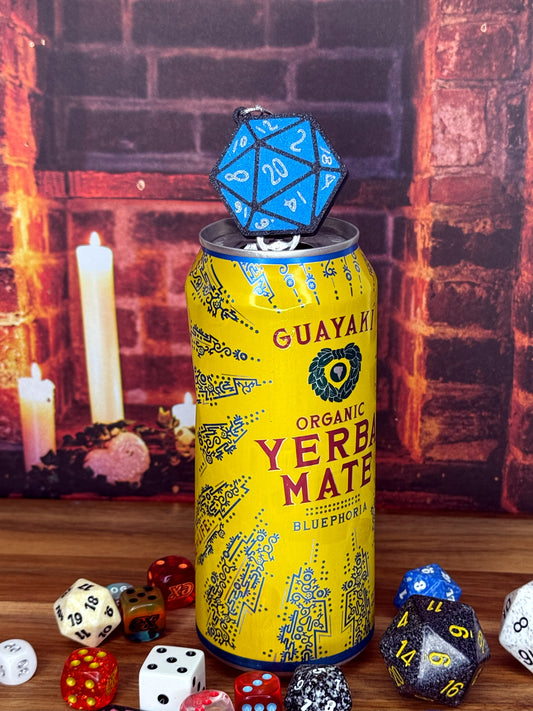 Yellow can of Guayaki Yerba Mate with a blue D20 Tab Buddy on top, surrounded by various dice on a wooden surface.