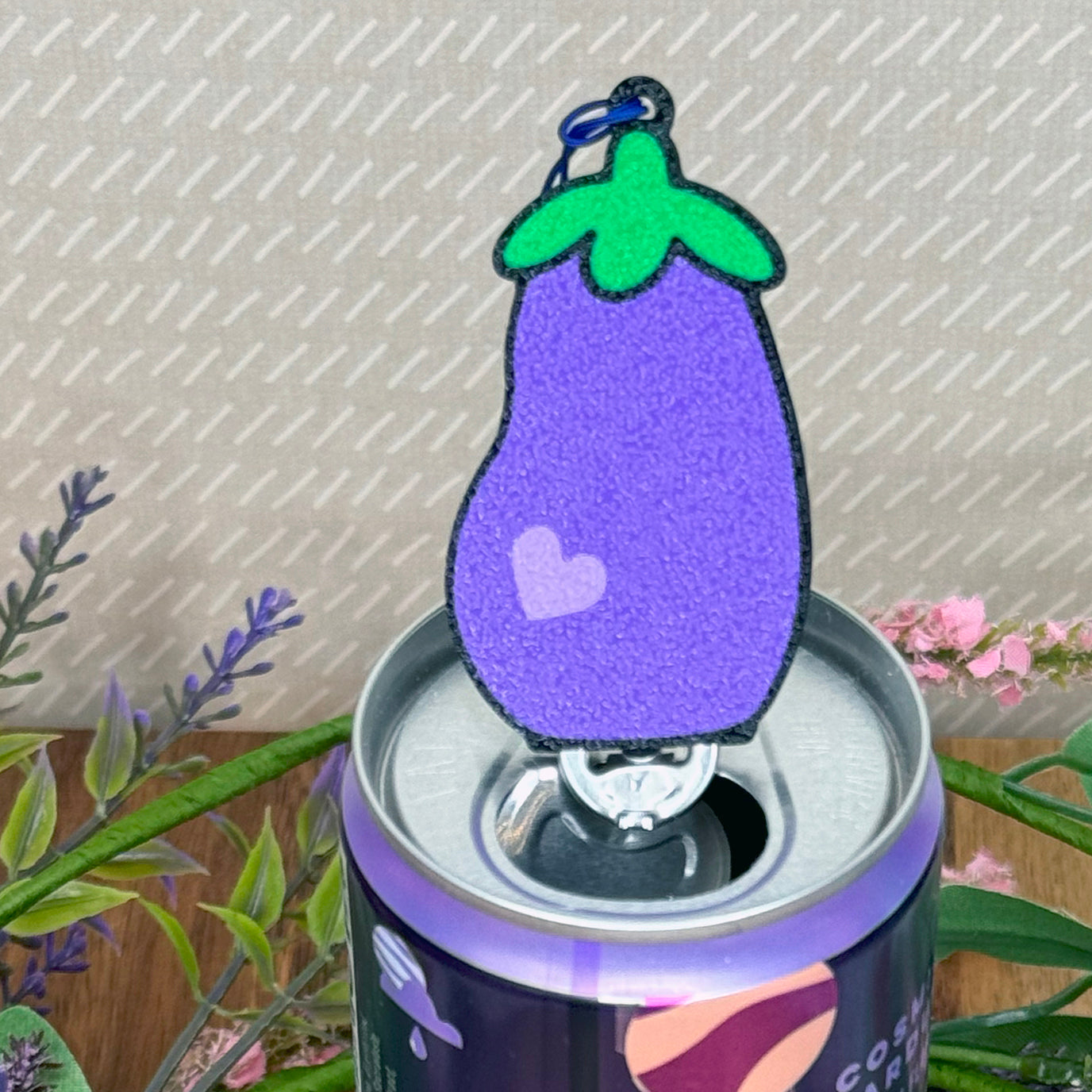Tab Buddy Keychain shaped like an eggplant on a can with plants in the background