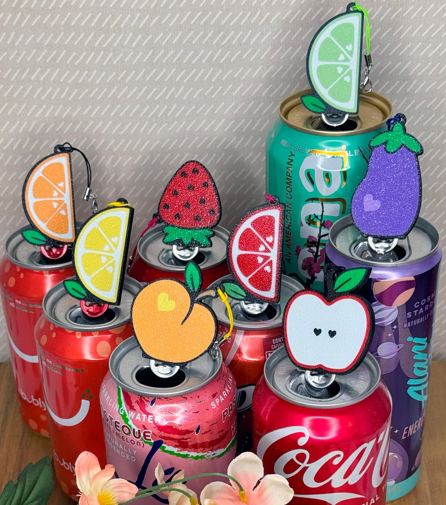 Collection of soda cans with fruit-themed Tab Buddies on a textured surface.