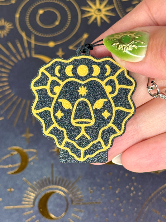 Hand holding a goldf and black Leo Zodiac Tab Buddy design against a background with celestial symbols.