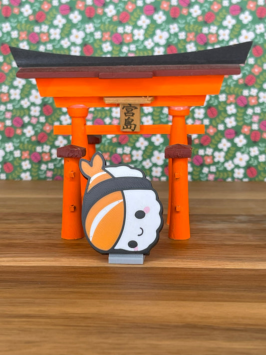 Cute nigiri-shaped Tab Buddy stands in front of an orange torii gate on a wooden surface with floral wallpaper.