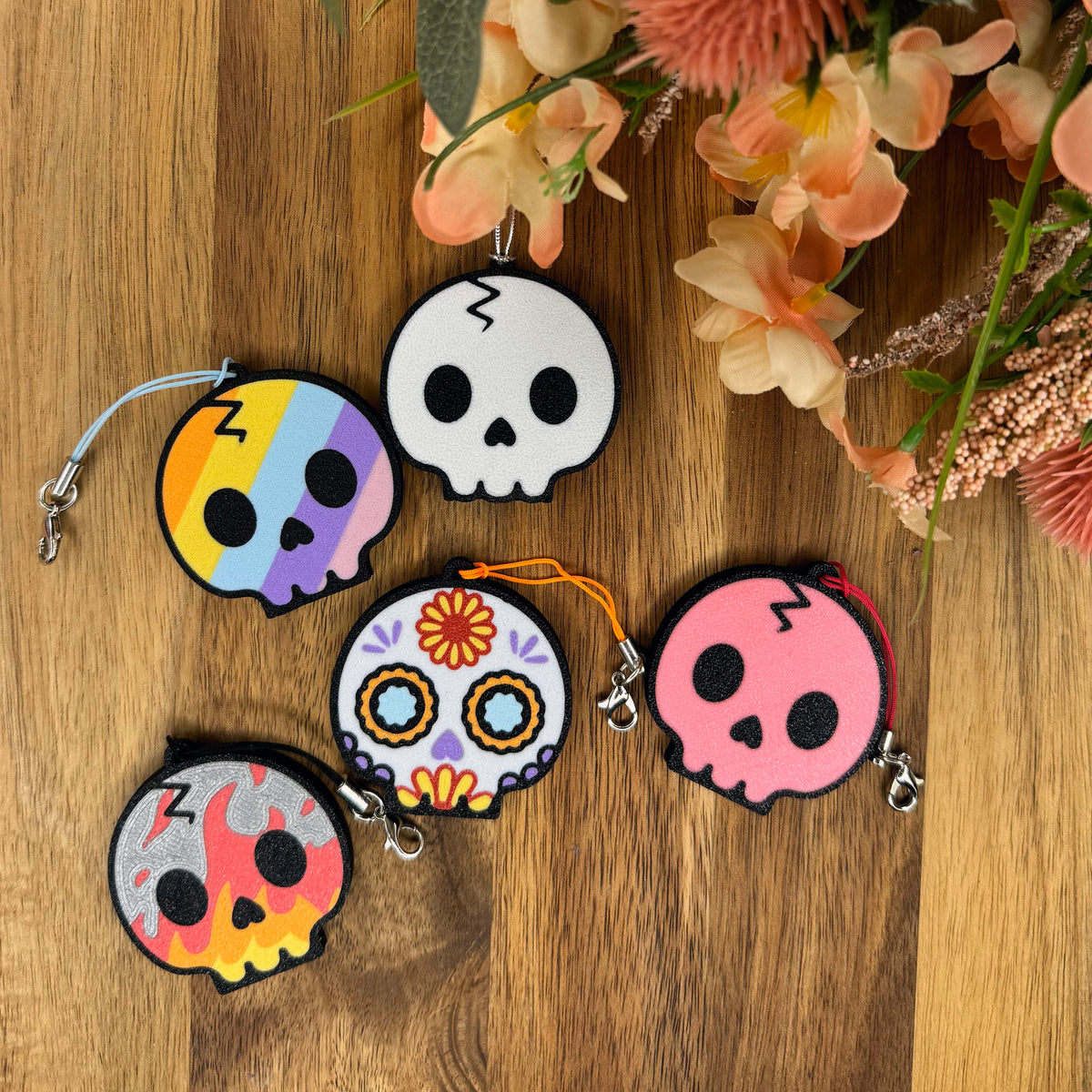 Five small skull-shaped Tab Buddies are arranged on a wooden surface with decorative flowers in the corner.