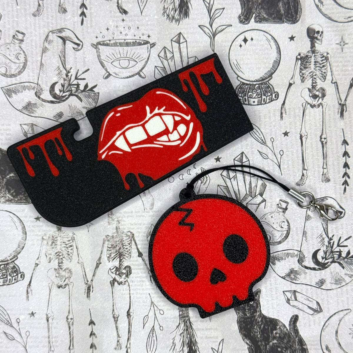 A black Vampire Lips Tab Buddy XL and limited run Red Skull soda-sized Tab Buddy rest againt a grey gothic background.
