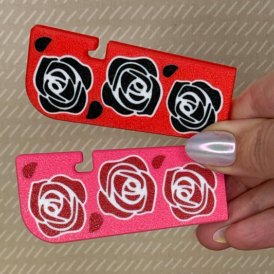Manicured hand holding two Tab Buddy XLs -- one red with black roses, and one pink with red roses.
