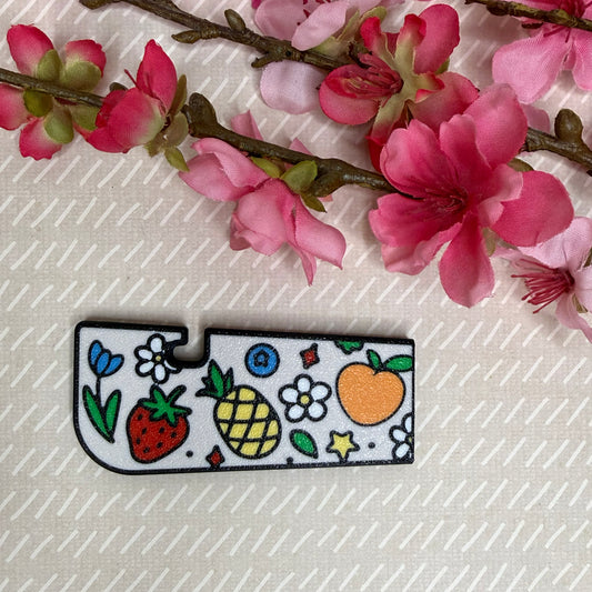A Tab Buddy XL in Fresh and Fruity design variation rests atop a beige surface with cherry blossom flowers in background.