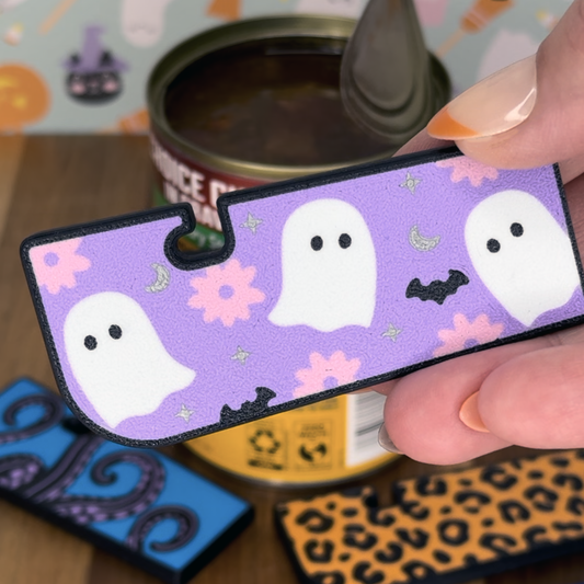 Halloween-themed Tab Buddy XL with ghosts and flowers on a purple background held by a hand over a can.