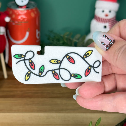 Hand holding a white Tab Buddy XL with Christmas lights design in front of a festive background.