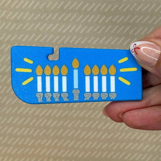 Blue Tab Buddy XL with a Hanukkah menorah design held by a hand against a beige background
