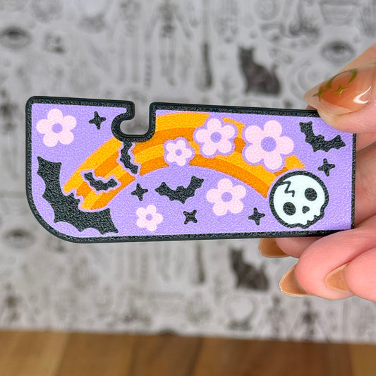 Decorative Tab Buddy XL with Halloween-themed orange rainbow, bat and skull design held by a hand against a neutral background