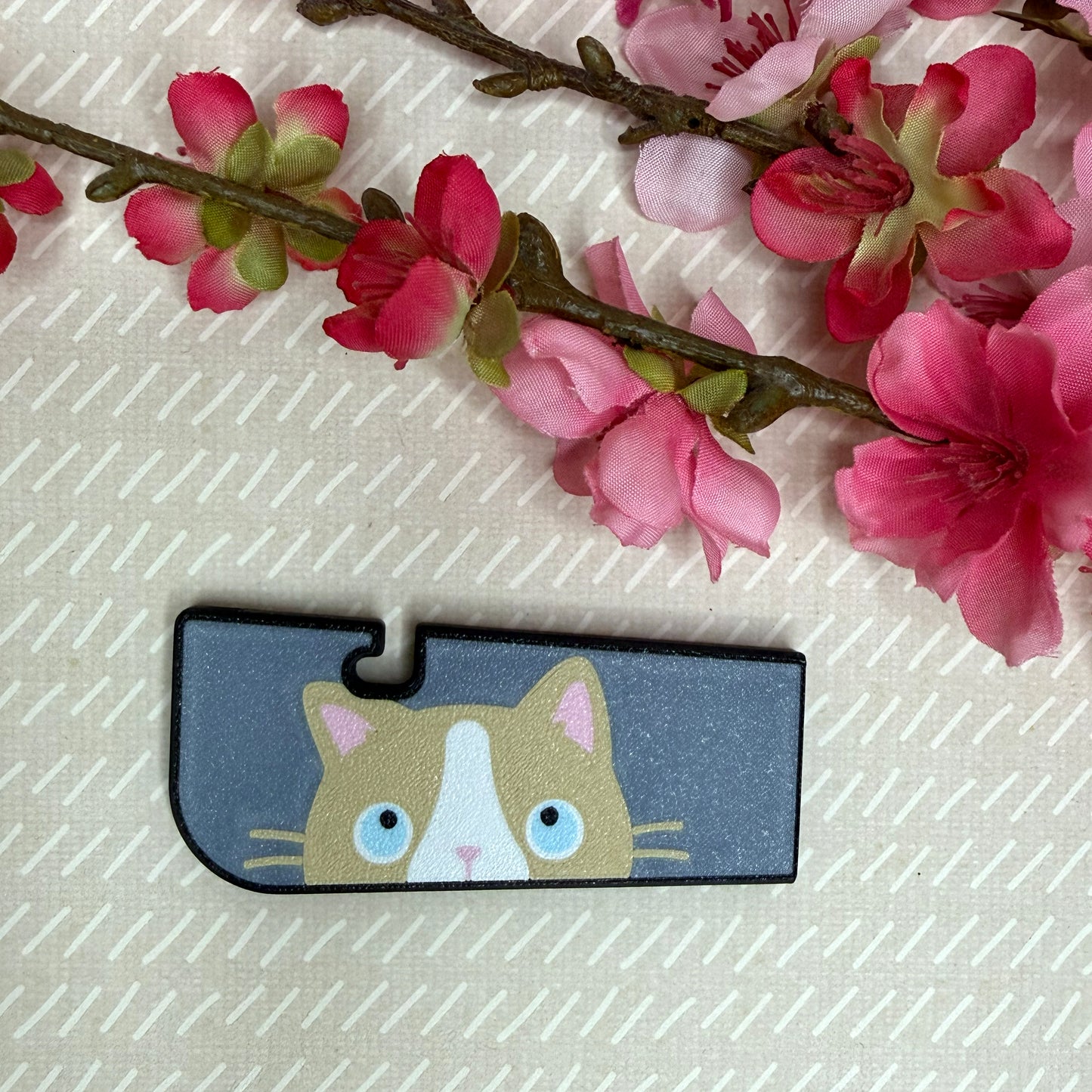 A Tab Buddy XL in Sneaky Ragdoll Cat color variation rests atop a beige surface with cherry blossom flowers in background.