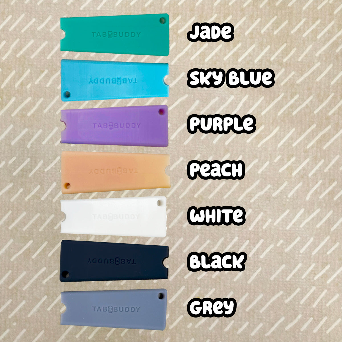 A vertical color-options display showing seven Tab Buddy Classics in different colors, labeled with text on the right: Jade, Sky Blue, Purple, Peach, White, Black, and Grey. The Tab Buddies are arranged on a textured beige background.