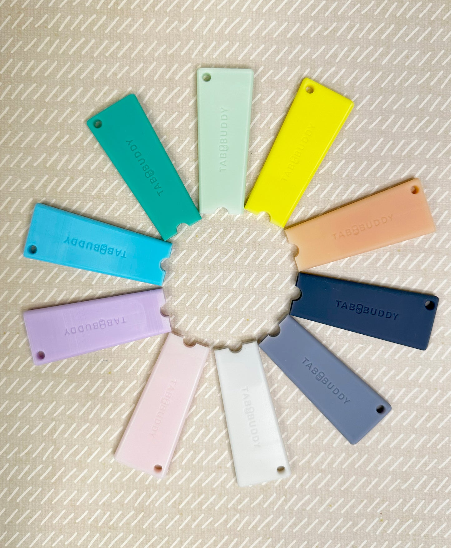 Tab Buddy Classic color swatches arranged in a circular pattern on a textured beige surface