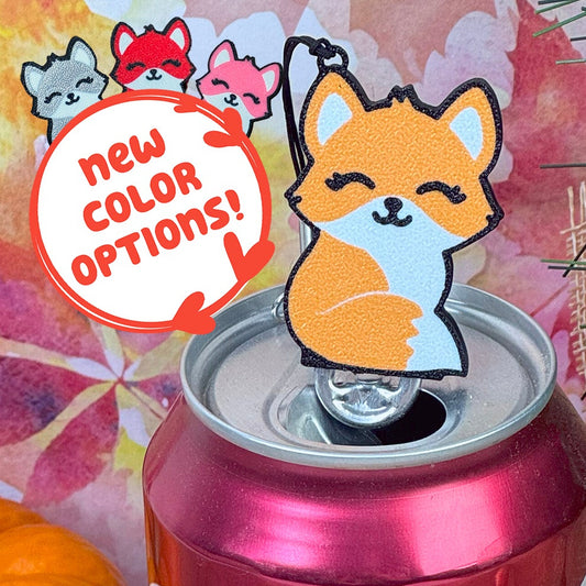 Soda can with an orange fox Tab Buddy on top, surrounded by pumpkins and autumn leaves. Text box reads "new color options!" with silver, red and pink foxes shown.