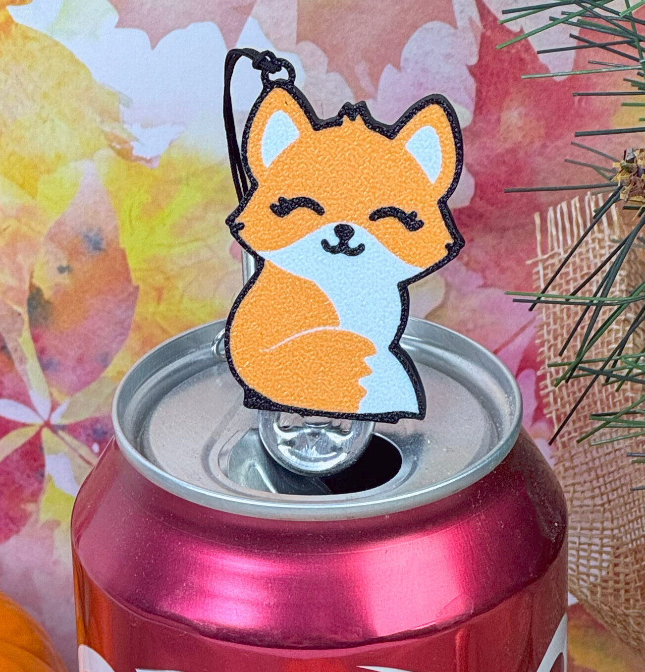 Orange fox-shaped Tab Buddy on a can with a fall foliage background