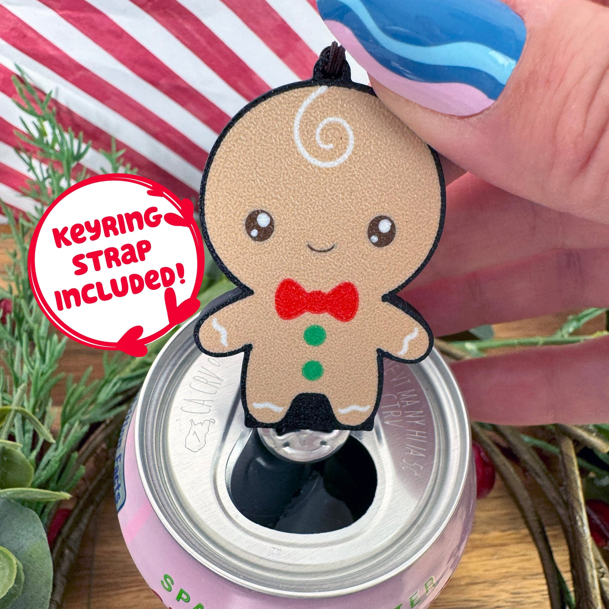 Gingerbread man Tab Buddy with keyring strap attached rests atop a soda can with festive background