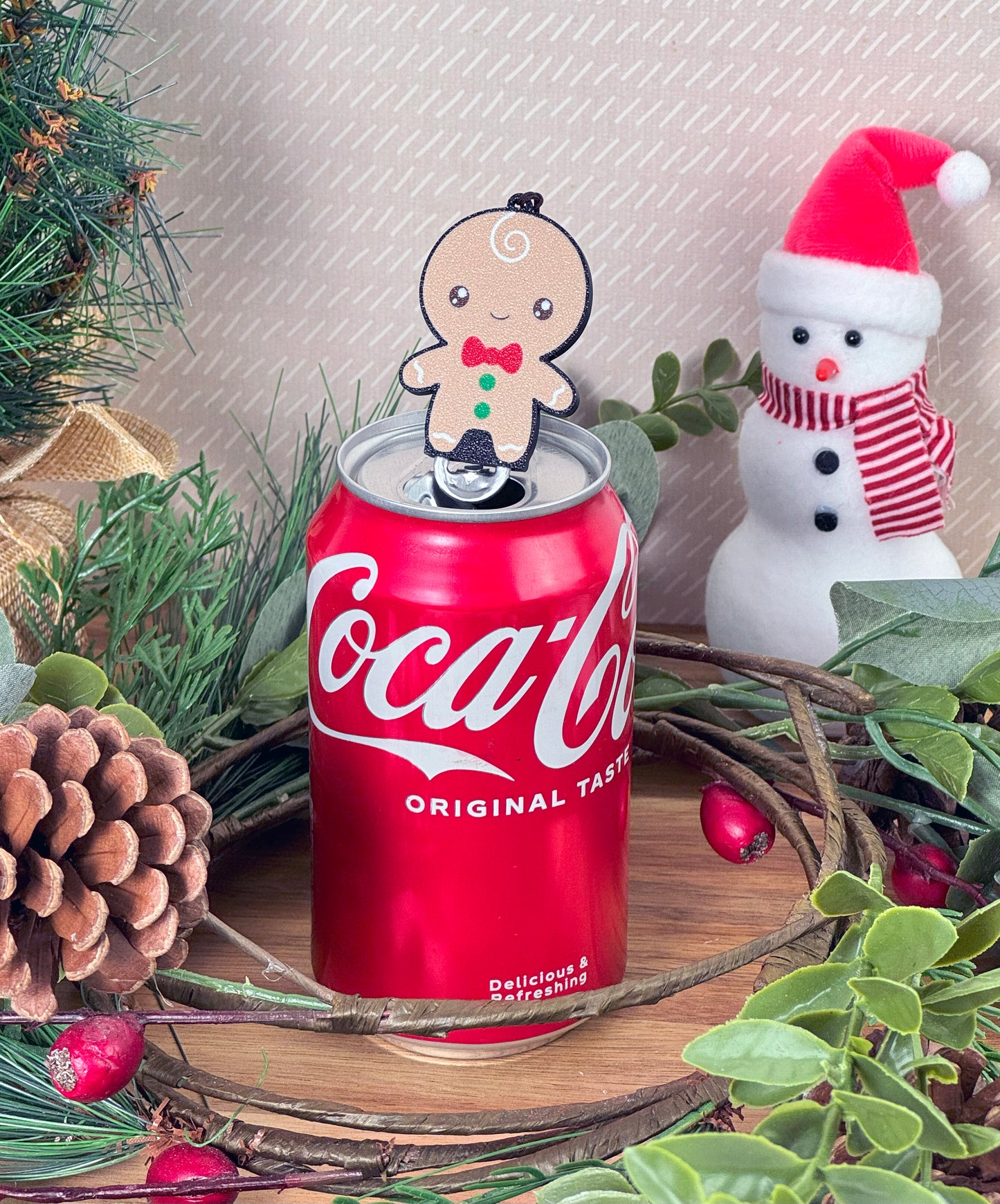 Coca-Cola can with a gingerbread man Tab Buddy on top, surrounded by Christmas decorations.