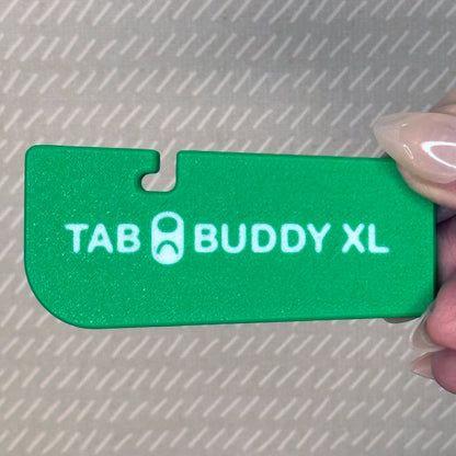Green 'TAB BUDDY XL' product held by a hand on a textured gray background