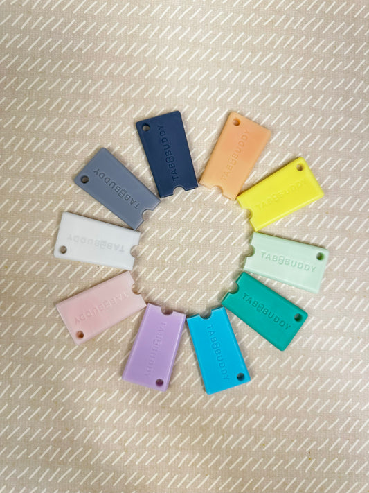 Colorful Tab Buddy Minis arranged in a circular pattern on a textured beige background