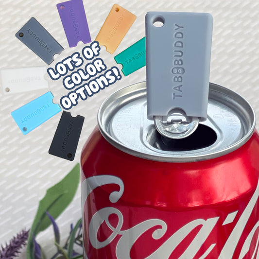 A grey Tab Buddy Mini rests atop a soda can after opening it. Text reads "Lots of color options!" with other color variations of the Tab Buddy Mini shown.