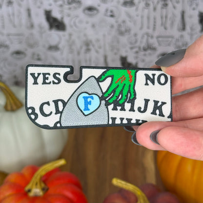 Halloween-themed yes/no label Ouija Tab Buddy XL with a hand holding it, surrounded by pumpkins.