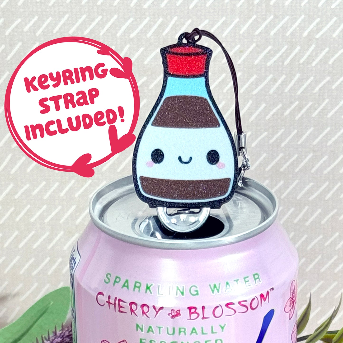 Soy sauce bottle-shaped Tab Buddy Keychain rests atop a sparkling water can 