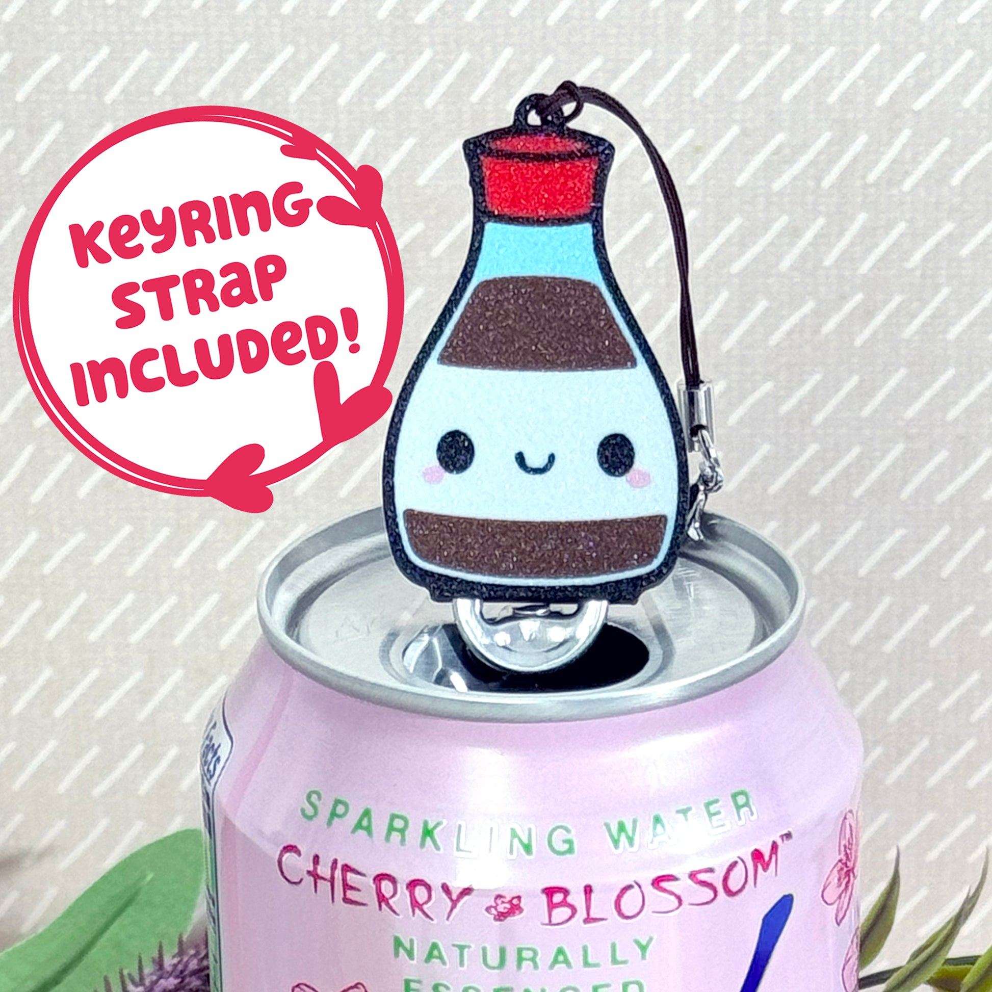 Soy sauce bottle-shaped Tab Buddy Keychain rests atop a sparkling water can 
