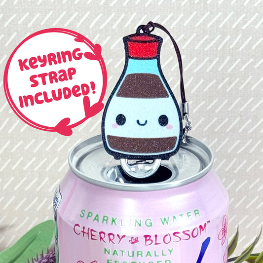 Soy sauce bottle-shaped Tab Buddy Keychain rests atop a sparkling water can 