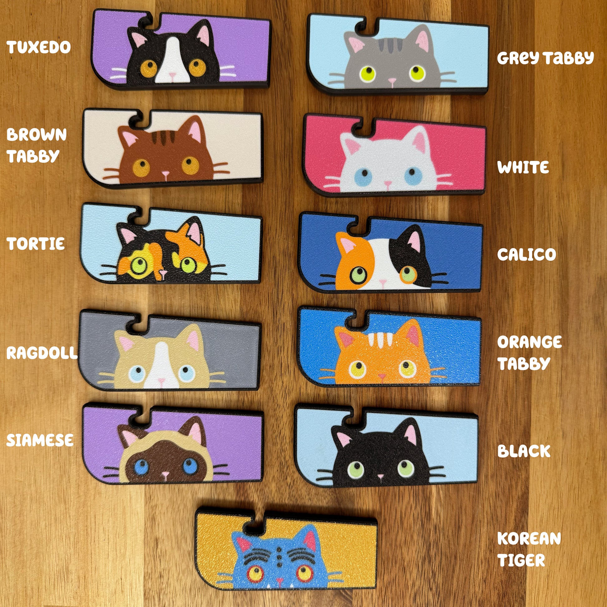 A color chart showing all current variations of the Tab Buddy XL sneaky cat. (Clockwise from top right): Grey Tabby, White, Calico, Orange Tabby, Black, Korean Tiger, Siamese, Ragdoll, Tortie, Brown Tabby, Tuxedo.