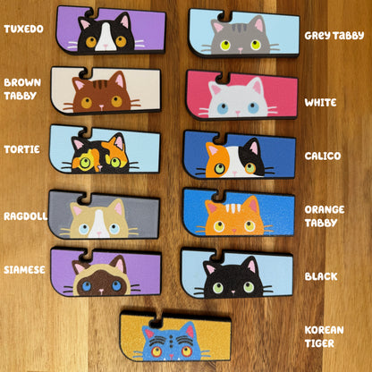 A color chart showing all current variations of the Tab Buddy XL sneaky cat. (Clockwise from top right): Grey Tabby, White, Calico, Orange Tabby, Black, Korean Tiger, Siamese, Ragdoll, Tortie, Brown Tabby, Tuxedo.