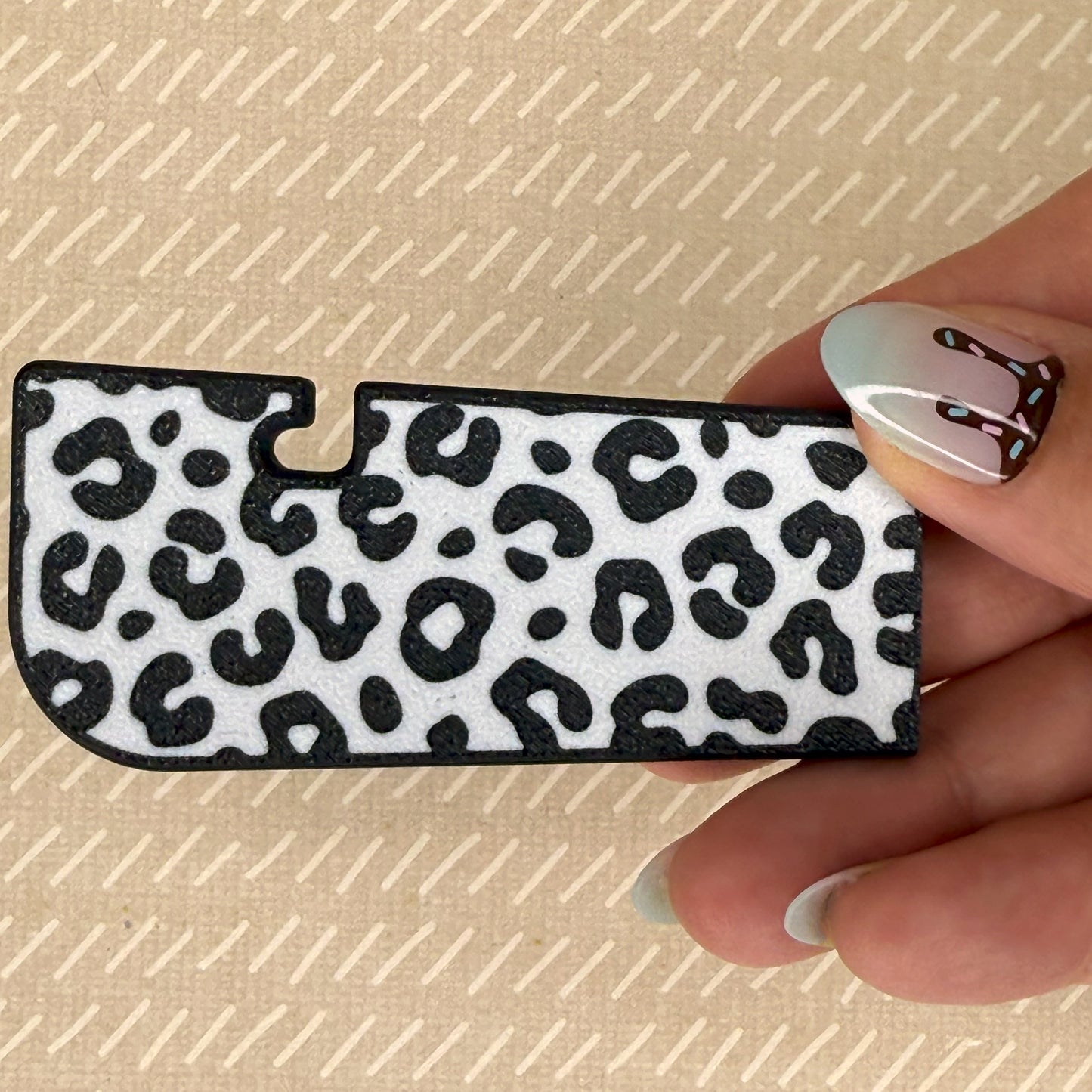 Hand holding a black and white leopard print Tab Buddy XL against a beige background