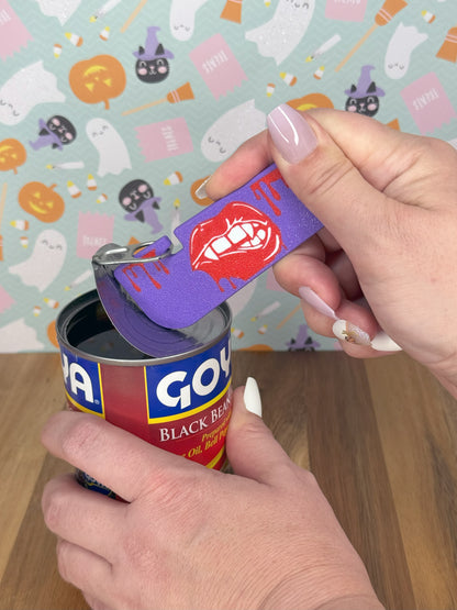 Hand holding Tab Buddy XL with a lips designs on it opening a can of Goya black beans with a Halloween-themed background