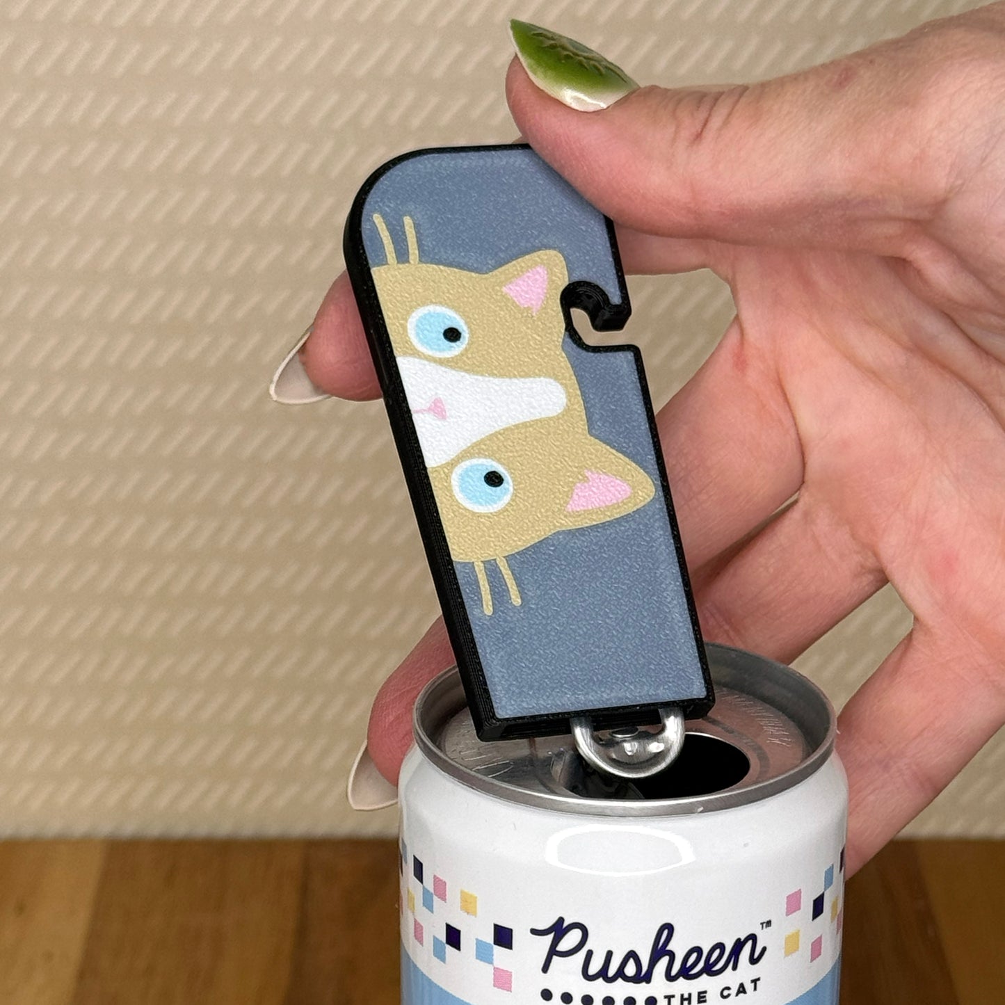 A ragdoll cat Tab Buddy XL is used to open a can of soda against a beige background and wooden surface.