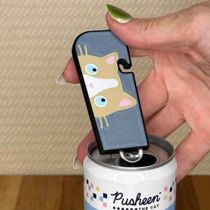 A ragdoll cat Tab Buddy XL is used to open a can of soda against a beige background and wooden surface.