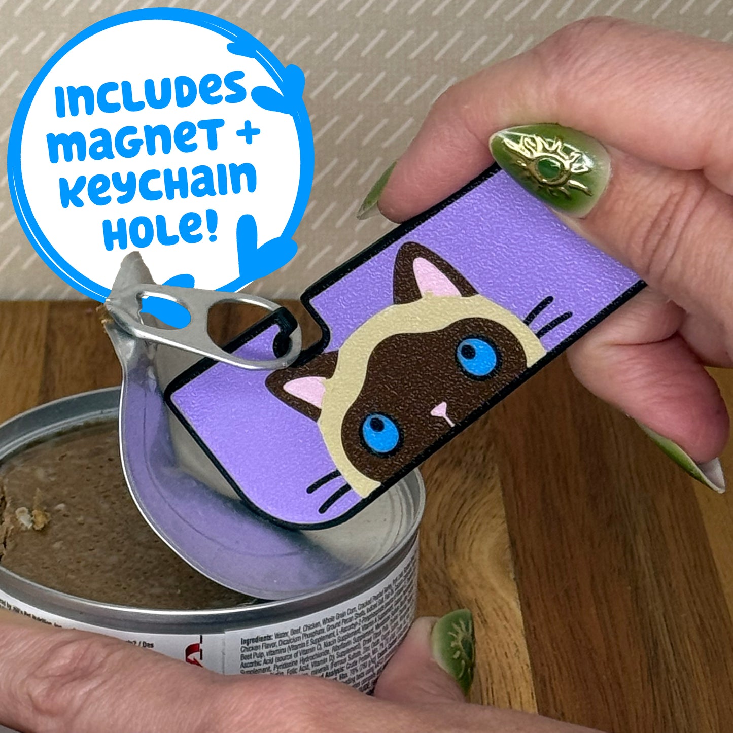 A Tab Buddy XL with a brown and tan siamese cat design is used to peel back the tab lid on a can of cat food. Text reads "Includes magnet + keychain hole!"
