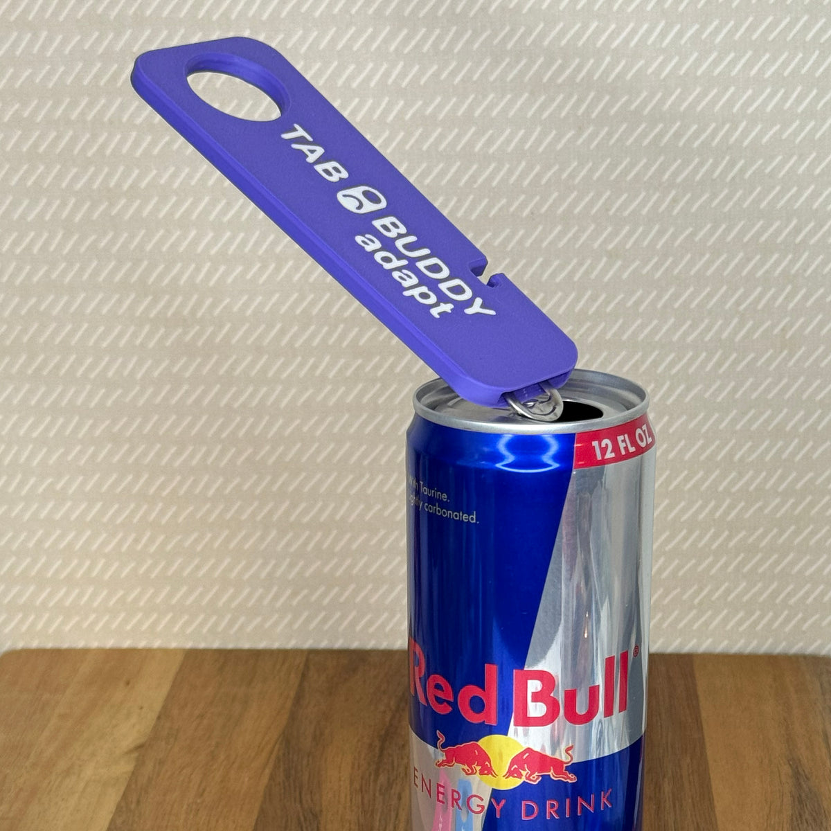 A purple Tab Buddy Adapt rests on the tab of a Red Bull can after popping it open.