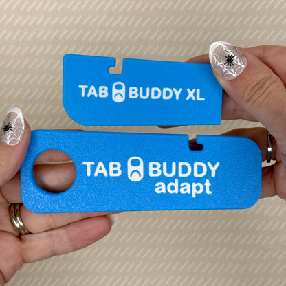 A sky blue Tab Buddy XL and Tab Buddy Adapt are shown side-by-side, emphasizing their size difference. The XL is 3 1/4 inches long, while the Adapt is 5 1/8 inches long and includes a grip assist hole.