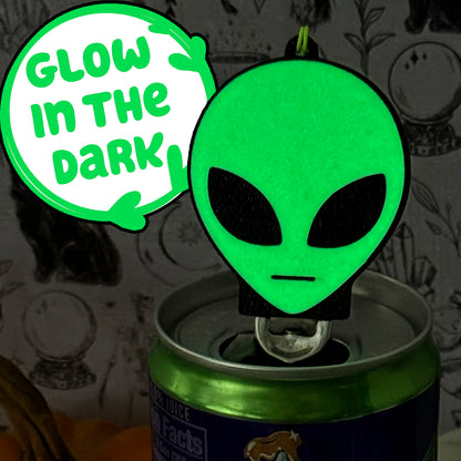 A glowing alien head Soda Tab Buddy rests atop a canned drink that has been popped open. Text bubble reads "Glow in the Dark."