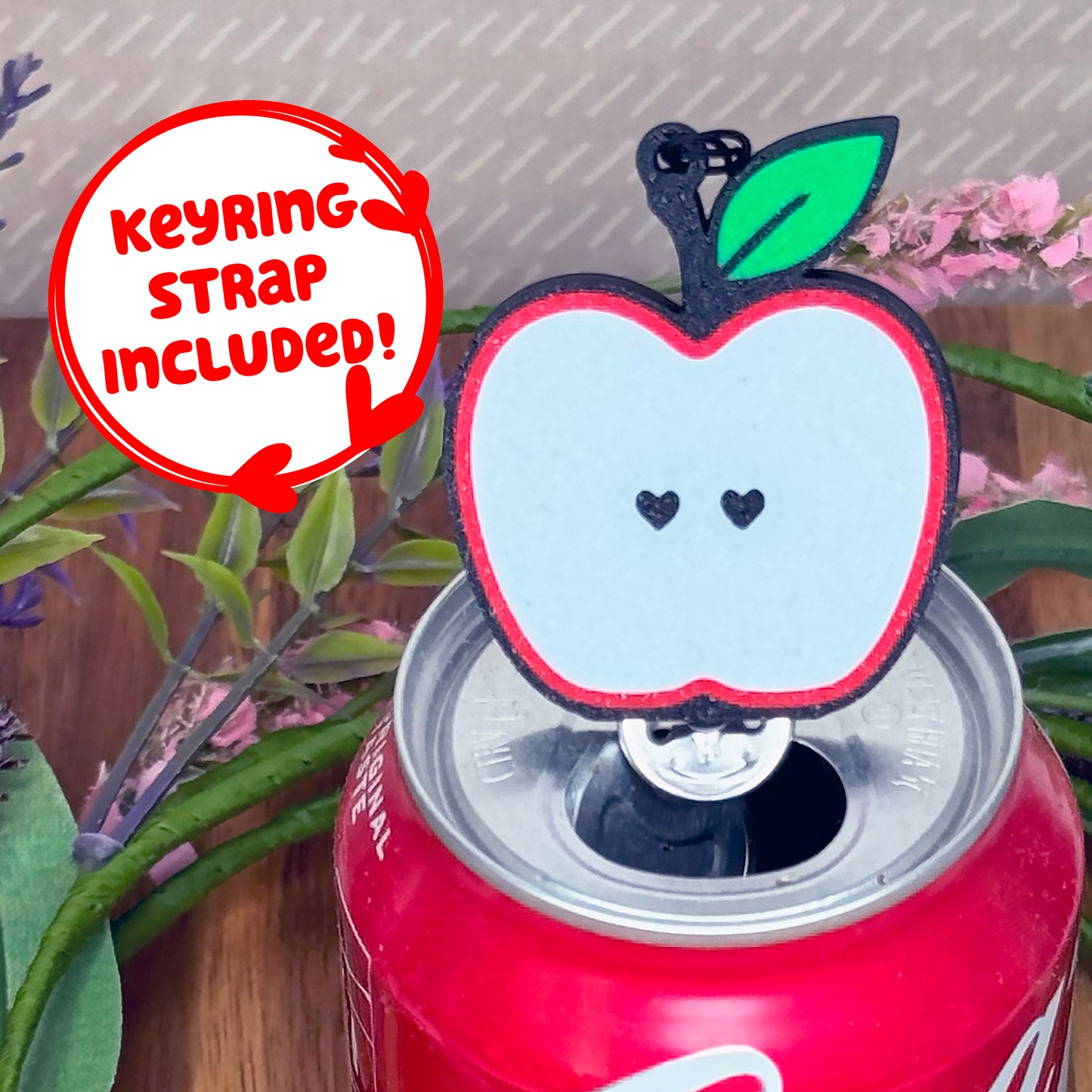 Apple-shaped Tab Buddy with keyring strap sits atop a can with plants in the background