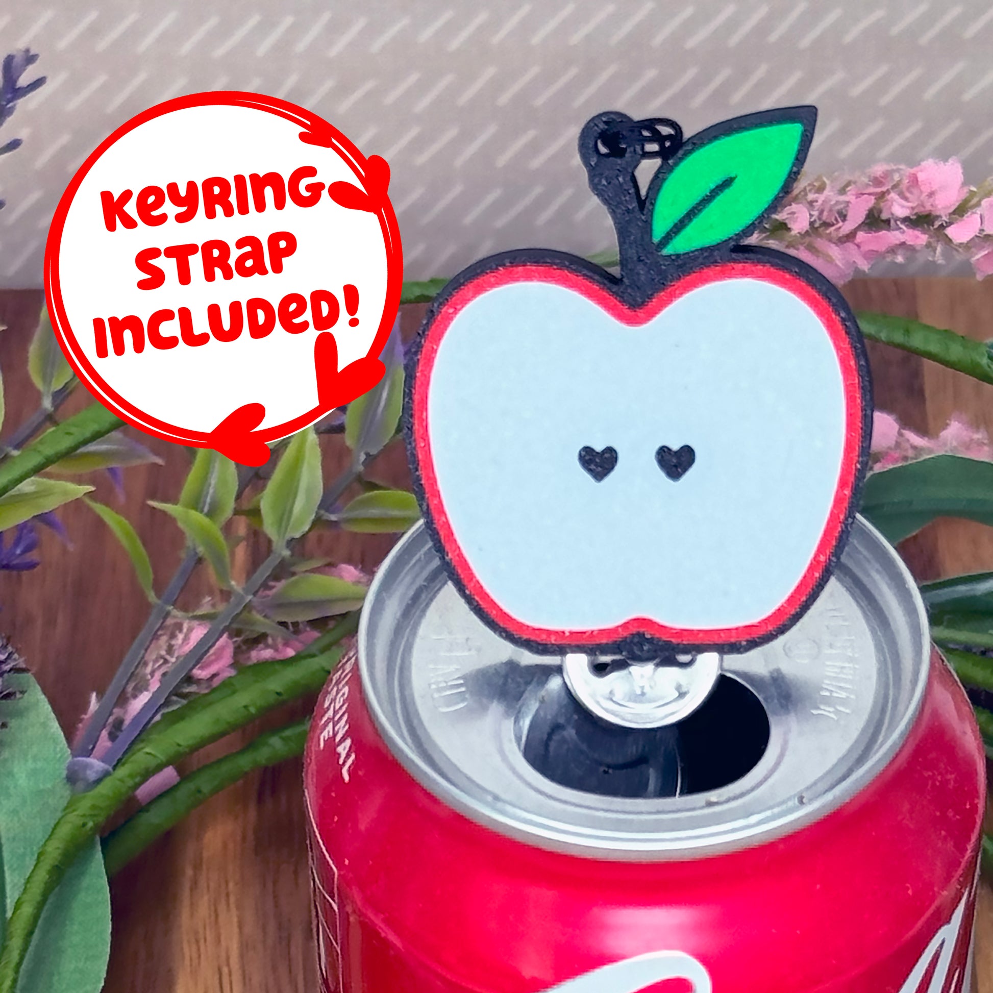 Apple-shaped Tab Buddy with keyring strap sits atop a can with plants in the background
