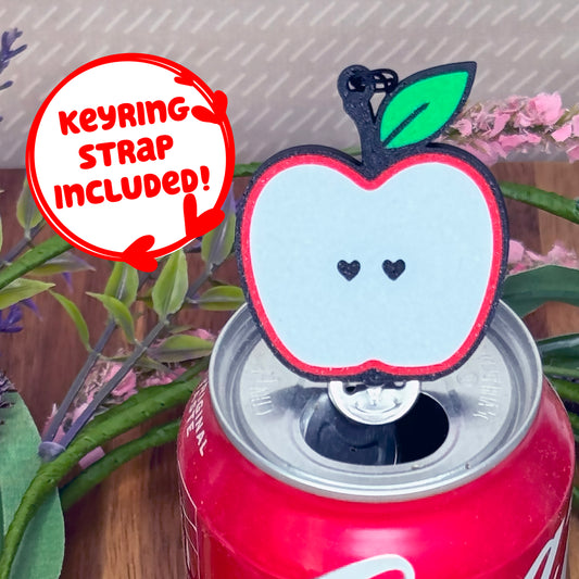 Apple-shaped Tab Buddy with keyring strap sits atop a can with plants in the background