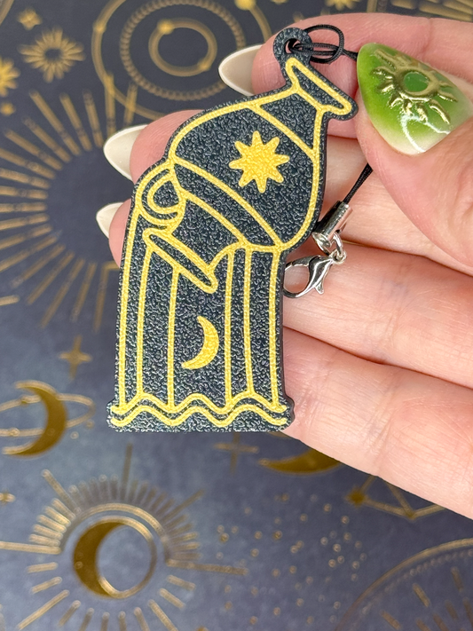 Hand holding a black and gold Aquarius Zodiac Tab Buddy keychain with celestial designs on a dark background.