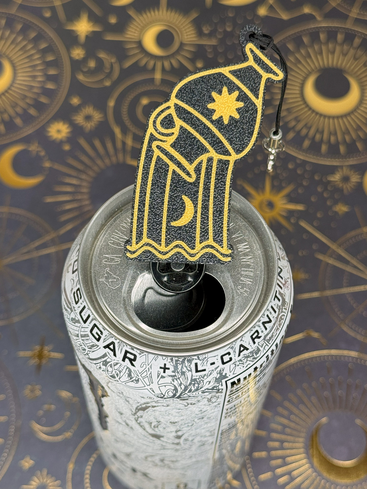 Decorative black and gold Aquarius Zodiac Tab Buddy keychain with a water bearer design sits on top of a can against an astrological symbol background