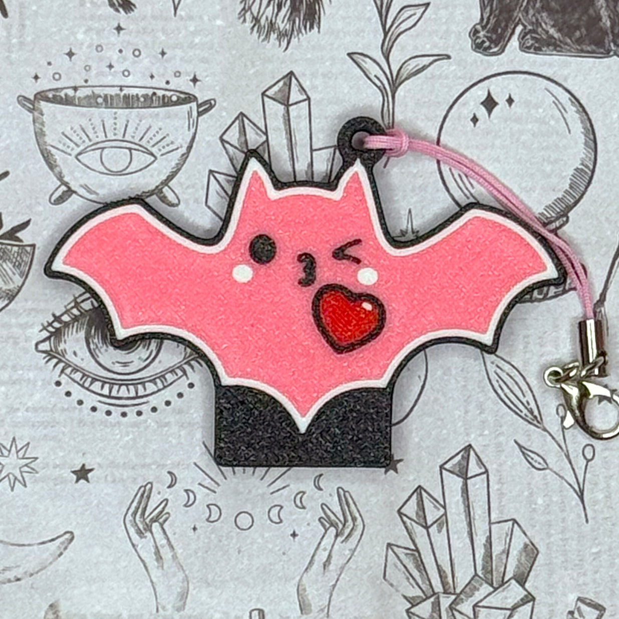Pink bat-shaped Tab Buddy with a heart on a gray background with illustrations