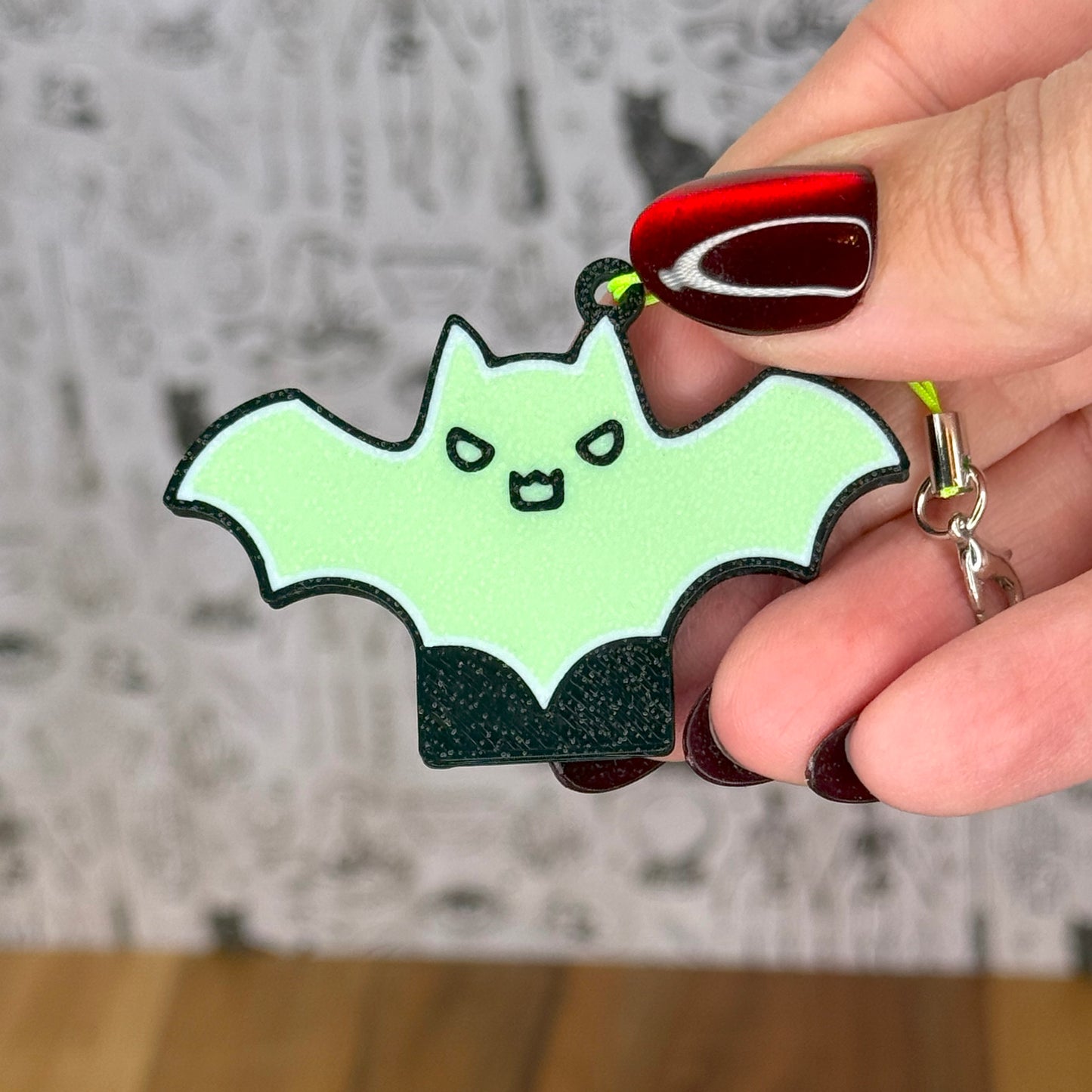 Hand holding a cute green bat-shaped Tab Buddy with a blurred background