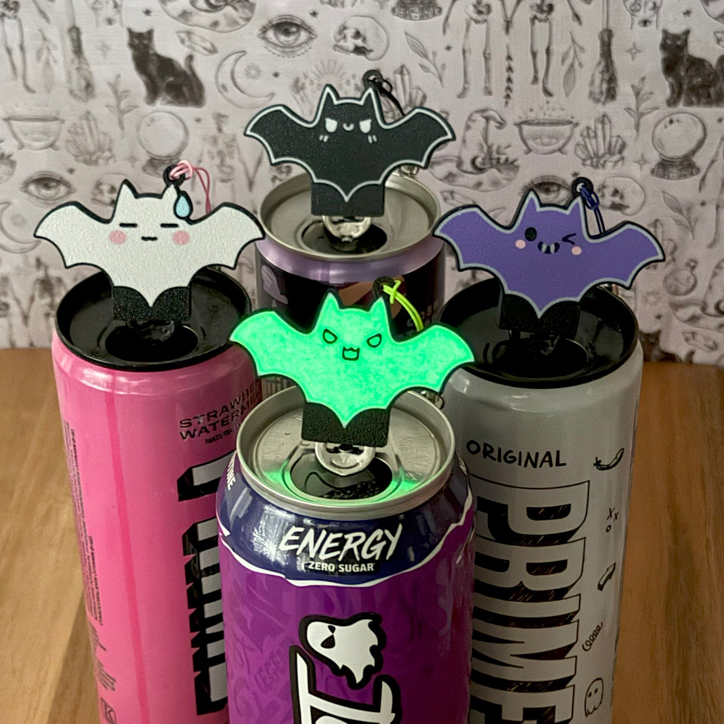 Four energy drink cans with bat-shaped Tab Buddies on a wooden surface.