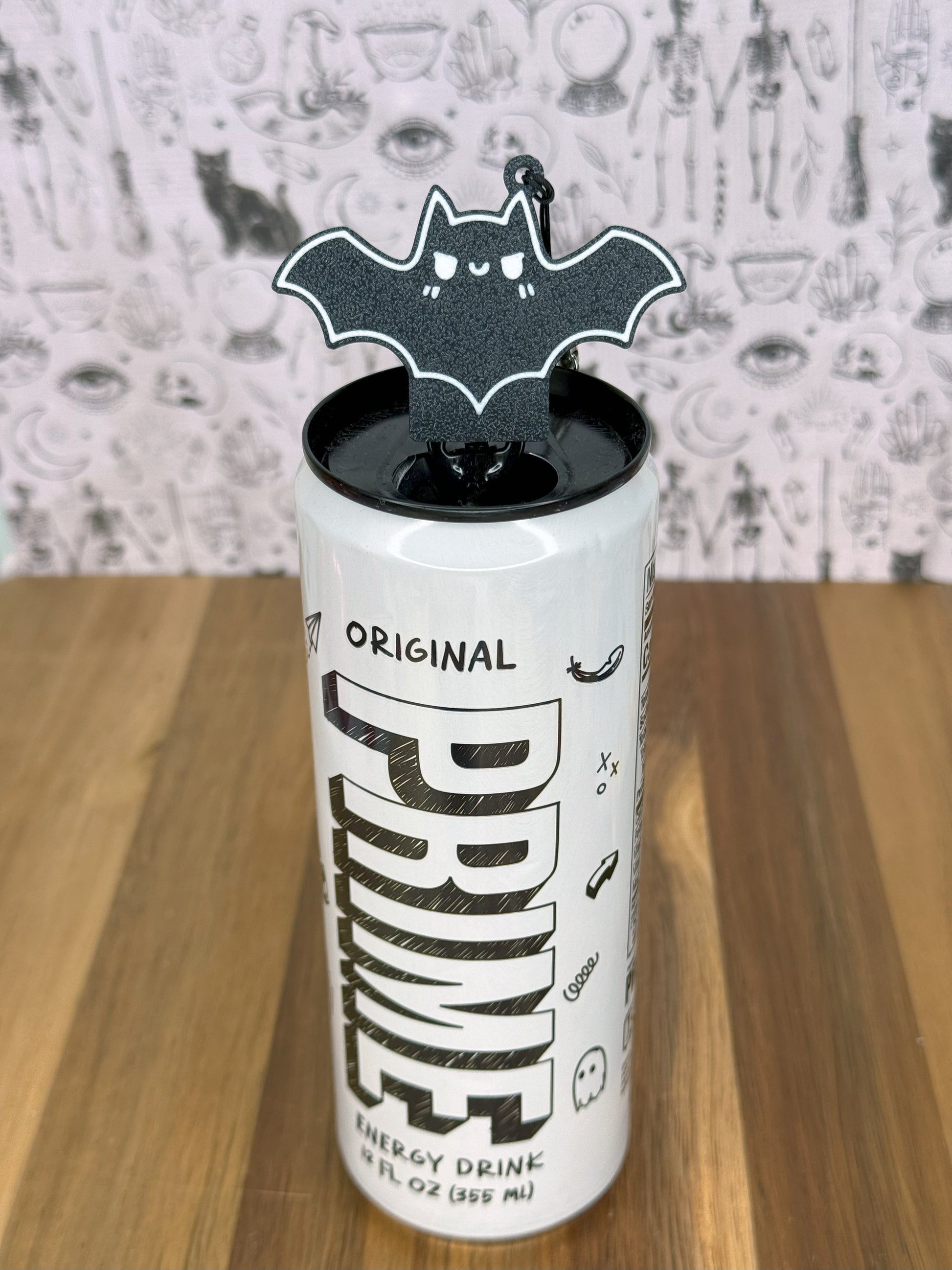 White energy drink can with black bat-shaped Tab Buddy on a wooden surface