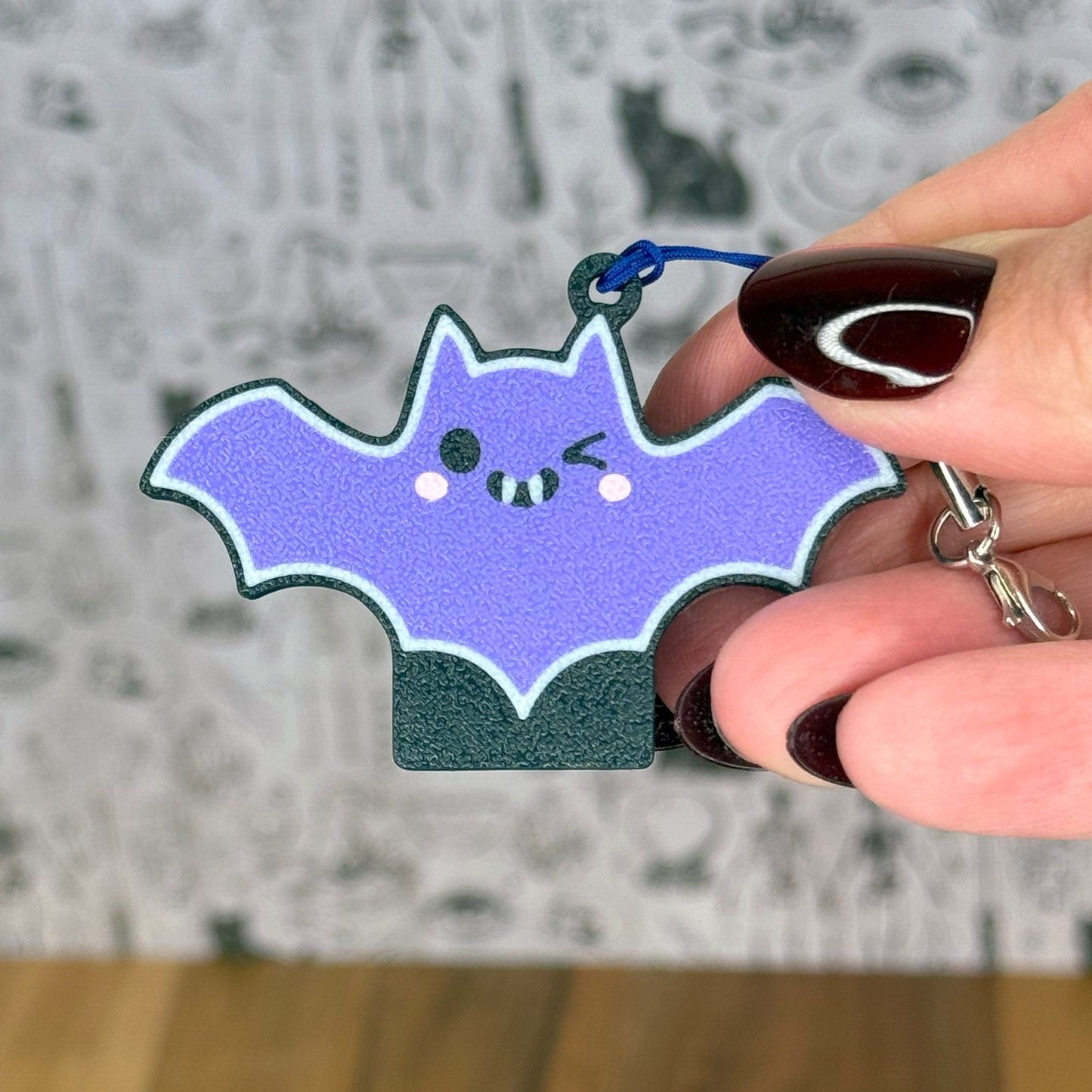 Hand holding a purple bat-shaped Tab Buddy with a smiley vampire face against a blurred background